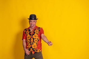 Havai gömleği ve melon şapkası giyen enerjik son sınıf öğrencisi sarı arka planda dans edip şarkı söylüyor.