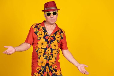 Hawaii gömleği giyen, güneş gözlüğü takan ve elleri parlak sarı arka planda olan son sınıf öğrencisi.