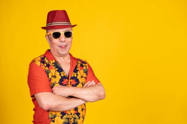 Güneş gözlüğü takan ve Hawaii gömleği giyen son sınıf öğrencisi parlak sarı bir arka planda çapraz kollarla dilini uzatıyor.