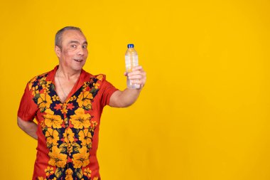 Kıdemli turist canlı bir Hawaii gömleği giyiyor, parlak sarı bir arka plana karşı bir şişe su sunuyor, hidrasyonu teşvik ediyor.