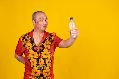 Neşeli, olgun bir adamın, ferahlatıcı bir şişe su tutarken, susuzluğu ve sağlıklı yaşam tarzını desteklerken çekilmiş bir fotoğraf.