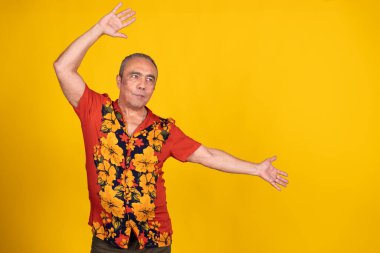 Havai tişörtü giymiş enerjik kıdemli bir adam özgürlüğün tadını çıkarıyor ve hayat dolu sarı bir arka planda kutluyor.