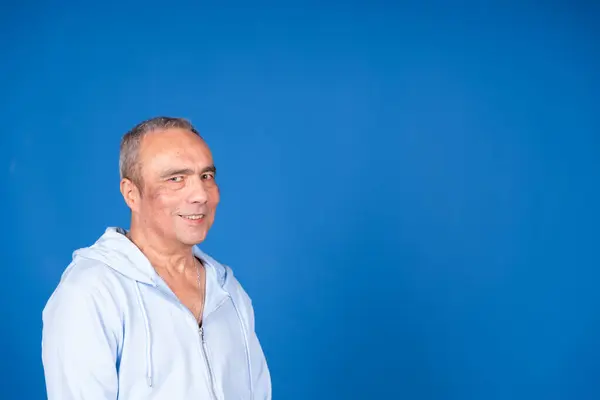 Neşeli bir son sınıf öğrencisinin portresi günlük kıyafetler giymiş, gülümseyen ve canlı mavi bir arka planda poz veren