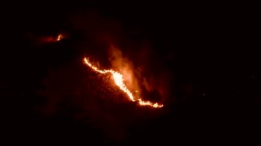Ormanda ateş ve dumanla gece yangını. Dumanı tüten bir alevin efsanevi hava videosu. Geceleri yanan, parlayan bir ateş. İklim değişikliği, ekoloji. Karanlıkta çizgi yangını..
