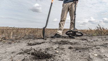 Metal dedektörüyle arkeolojik ve hazine avcılığı. Yeraltında antika arayışı. Altın külçeleri üzerinde toprak araştırması. Elinde metal dedektörü ve küreği olan bir adam.