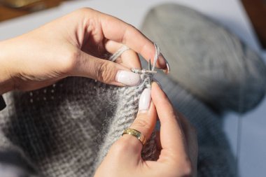 Close up hands knitting the dress from light blue wool on blurry background. Using circular needles