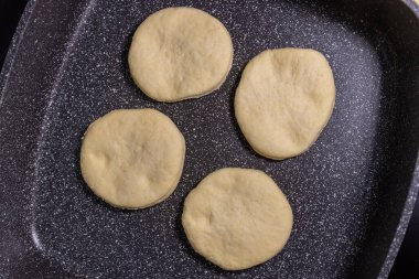 Raw flatbread dough pieces placed in a non-stick pan, ready for cooking. clipart