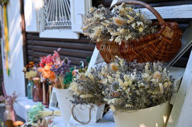 in the reflections of the bright sun a small cozy flower shop with baskets of dried herbs, flowers and vases with multi-colored field ears near it. clipart