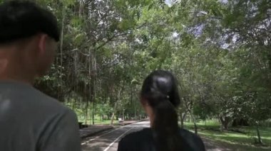 İki Asyalı genç doğa parkında sokakta birlikte rahatça yürüyor. Dikiz aynasından takip edin. Oğlan ve kız. Arkadaşlık. Açık hava takibi. Yavaş çekim.