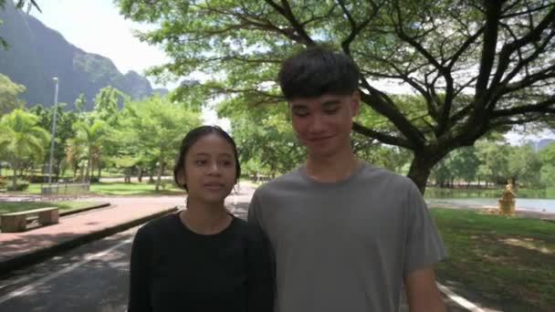 两名身穿休闲装的亚洲少年在公园的街上散步聊天 青少年的生活方式 户外追捕 同学的友谊 男孩和女孩 暑期约会 — 图库视频影像