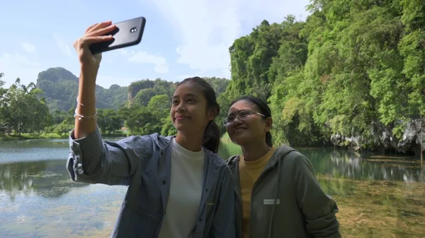 Asian adorable teen girl and her mom taking selfie photo together with beautiful scenery of the marsh in the green valley during summer. Outdoor pursuits. Bonding moment in family.