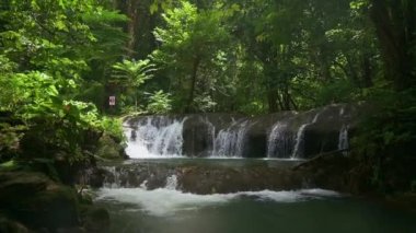 Yağmur ormanlarında sabah güneşinin altında yeşil bitki örtüsüyle çevrili güzel bir şelale manzarası. Ağır çekimle kaldırıyorum. Sa Nang Manora Şelalesi. Phang Nga Eyaleti. Tayland.
