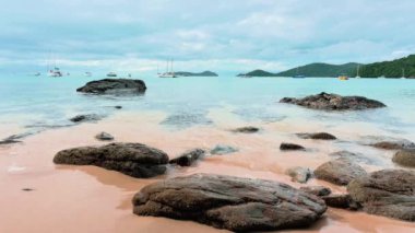 Phuket, Tayland 'da bulutlu mavi gökyüzünün altında berrak, güzel bir sahil manzarası. Deniz suyu, deniz kıyısında kayaların üzerinde yavaşça süzülüyor. Birçok yat kıyıya yakın yüzer..