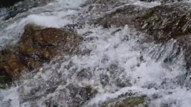 Şelaleden akan hızlı su akıntısı güneş ışığı altındaki kayalıklara doğru akıyor. Taze temiz su arkaplanı.