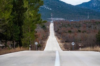 Bulutlu bir günde asfalt yol manzarası. Dramatik bulutlu gökyüzünün altındaki ormanda yol. Göz alabildiğine uzanan asfalt bir otoyolu olan geniş, açık çayır görüntüsü..