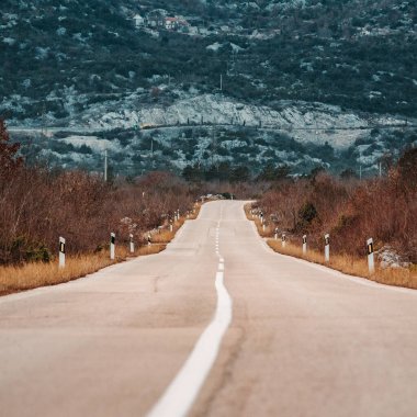 Bulutlu bir günde asfalt yol manzarası. Dramatik bulutlu gökyüzünün altındaki ormanda yol. Göz alabildiğine uzanan asfalt bir otoyolu olan geniş, açık çayır görüntüsü..