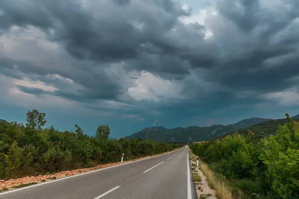 Bulutlu bir günde asfalt yol manzarası. Dramatik bulutlu gökyüzünün altındaki ormanda yol. Göz alabildiğine uzanan asfalt bir otoyolu olan geniş, açık çayır görüntüsü..