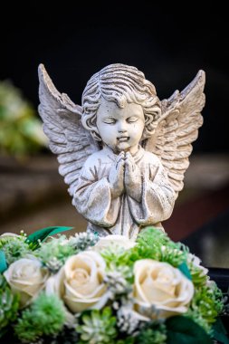 Weathered Angel Statue in Prayer Surrounded by Elegant Floral Arrangement clipart