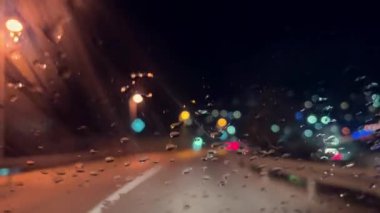 Yağmurlu bir gecede Renkli Bokeh Işıkları Yağmur damlalarıyla bir arabanın ön camından görülüyor