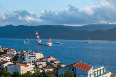 KOMARNA, CROATIA - 9 Ekim 2019: Peljesac Köprüsü şantiyesi, vinci ve Adriyatik Denizi 'ndeki gemileri olan yerleşim köyü Komarna' nın görüntüsü