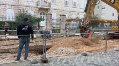 METKOVIC, CROATIA - 11 Aralık 2024: Tarihi bir taş binanın yakınındaki kazıcı ve işçilerin güvenlik donanımlı olduğu inşaat alanı. Kentsel yenilenme sırasında şehir merkezinde inşaat alanı