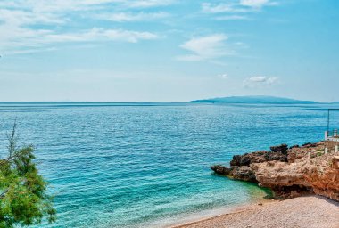 Hırvatistan 'daki Peljesac Yarımadası' nın Sahra Sahili 'nde Adriyatik Denizi ve Dingac Bölgesi' ndeki Rocky Shoreline yer alıyor. Kristal berrak deniz, gökyüzü ve sahil.