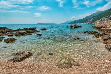 Hırvatistan 'daki Peljesac Yarımadası' nın Sahra Sahili 'nde Adriyatik Denizi ve Dingac Bölgesi' ndeki Rocky Shoreline yer alıyor. Kristal berrak deniz, gökyüzü ve sahil.