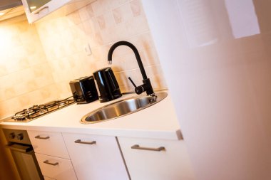 Yuvarlak lavabolu modern beyaz mutfak, siyah musluk ve konforlu apartman ortamında uyumlu siyah aletler.