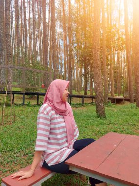 Genç bir kadın çam ormanında ceket giyiyor, çam ormanının egzotik doğasının tadını çıkarıyor, mesai saatleri dışında dinleniyor.