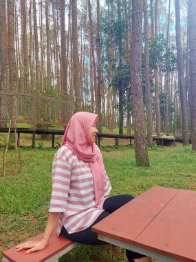 Genç bir kadın çam ormanında ceket giyiyor, çam ormanının egzotik doğasının tadını çıkarıyor, mesai saatleri dışında dinleniyor.