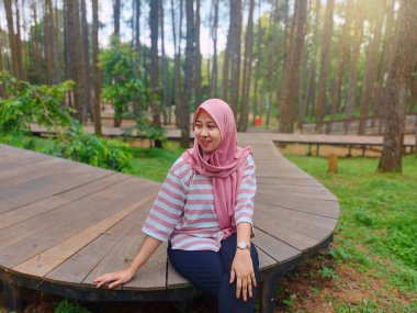 Genç bir kadın çam ormanında ceket giyiyor, çam ormanının egzotik doğasının tadını çıkarıyor, mesai saatleri dışında dinleniyor.