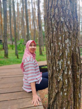 Genç bir kadın çam ormanında ceket giyiyor, çam ormanının egzotik doğasının tadını çıkarıyor, mesai saatleri dışında dinleniyor.