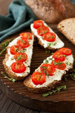 Makarnalı tost ekmeği, krem peynirli ve domatesli. Ahşap arka planda basit bir köy kahvaltısı.