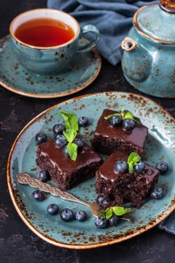 Yaban mersinli çikolatalı kek ve koyu beton arka planda çaydanlıklı çay fincanı.