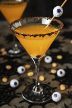 Cadılar Bayramı turuncu kokteyli. İçki konsepti, karanlık arka planda tatil süslemeleri olan bardaklar.