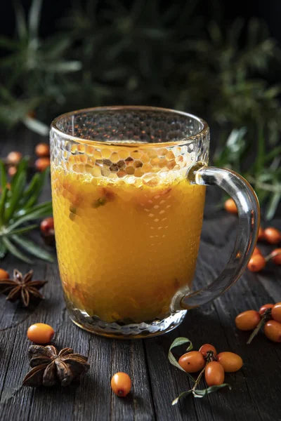 Hot spicy tea with sea buckthorn in glass cup on dark background, selective focus