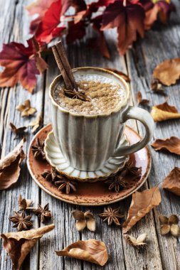 Bir kupa sonbahar balkabaklı latte, krema ve baharatlı. Kabaklı kahve ve ahşap arka planda tarçın.