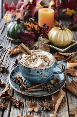 Bir kupa sonbahar balkabaklı latte, krema ve baharatlı. Kabaklı kahve ve ahşap arka planda tarçın.
