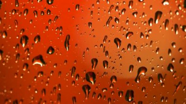 Soğuk gecelerde pencereye turuncu arka planda yağmur damlaları düşer. Yağmurlu karamsar bir arka plan. Yağmur damlaları kayıyor.