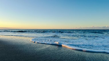 Altın saatinde mavi okyanus dalgaları. Gün batımında yumuşak ışığa sarılmış okyanus dalgaları. Gezginler ve hayalperestler için sakinleştirici bir fotoğraf.