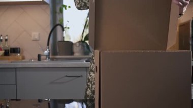 Kadın mutfak masasına karton bir kutu yerleştiriyor, paketleme ya da depolama için hazırlanıyor. Organizasyon, taşınma veya ev hazırlama kavramı