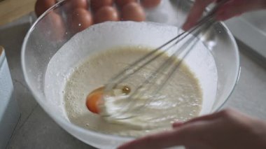 Çiğ yumurtayı krep hamuruna karıştırmak için çırpıcıyı kullanan el.
