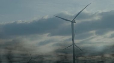 Rüzgar türbinleri hareket halindeki araçtan yakalanan bulutlu gökyüzüne karşı döner. Yenilenebilir enerji, rüzgar enerjisi ve çevre dostu elektrik üretimi