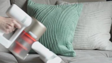 Elektrik süpürgesi yeşil ve bej yastıkların yakınındaki koltuğun tozunu alıyor.