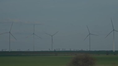 Hareket eden bir perspektiften bakıldığında, birkaç rüzgar türbini yeşil bir alanda döner.