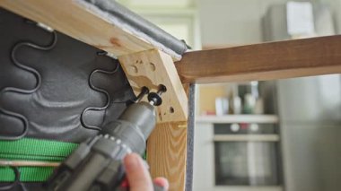 Elektrikli matkap kullanan bir kadın sandalyeye bağlı bacağı çerçevelemek için