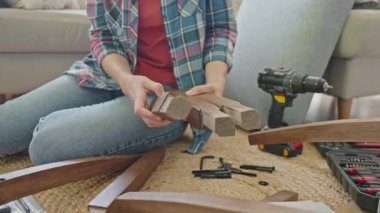 Üç tahta bacağı tutan ve teftiş eden kadın montaj sırasında yerde oturuyor.
