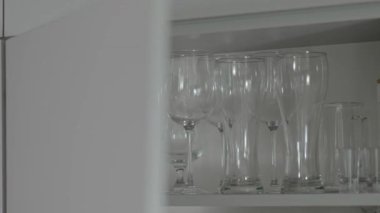 Kadın cam eşyalar ile dolu bir raftan iki şarap kadehi alır.