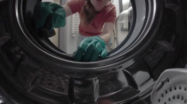 Eldivenli kadın çamaşır makinesi davulunu içeriden temizliyor.