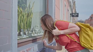 Kadın mücevher sergisini yakından incelemek için vitrine doğru eğiliyor.